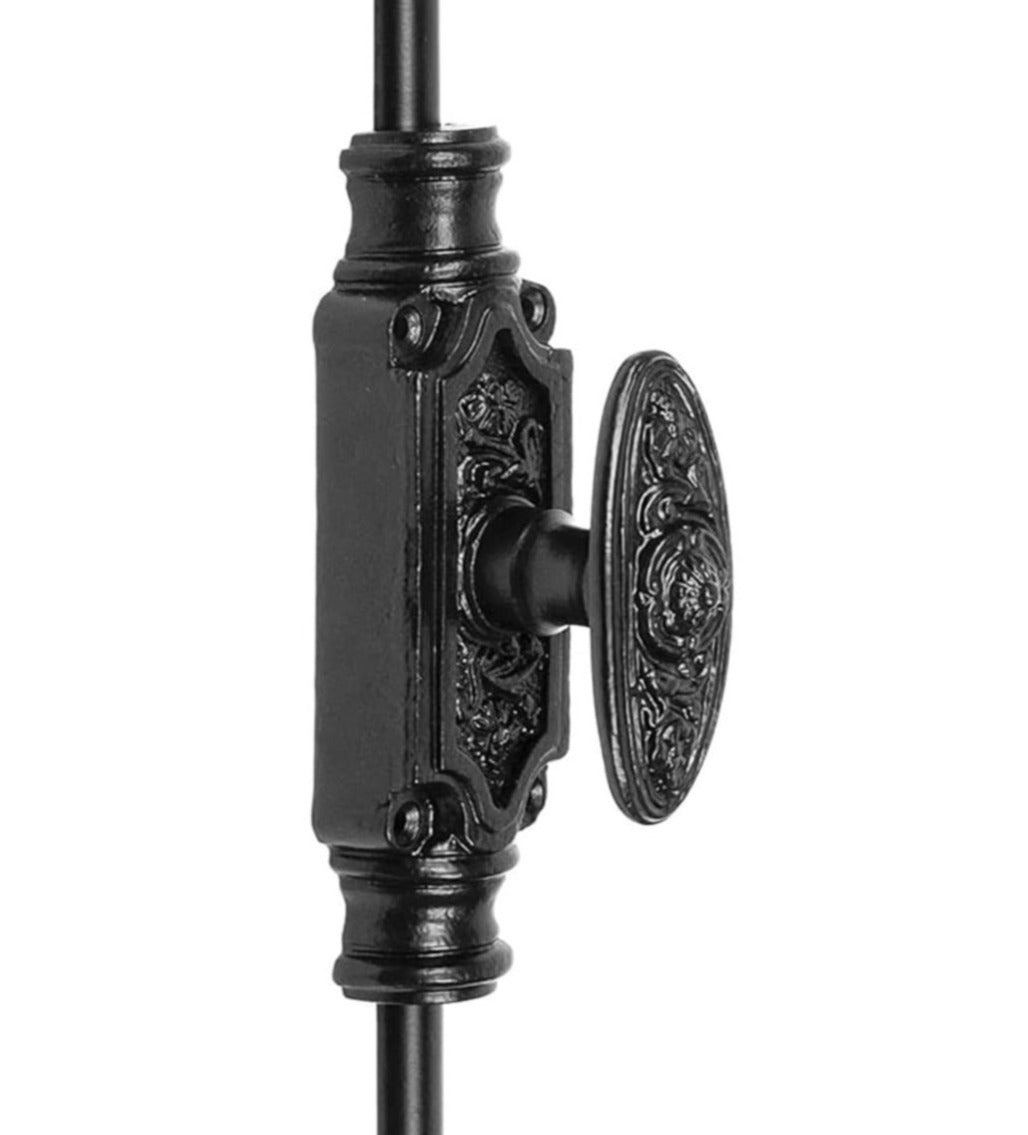 A black powder coated iron cremone bolt for doors, featuring a decorative center plate with a knob and ornate detailing.